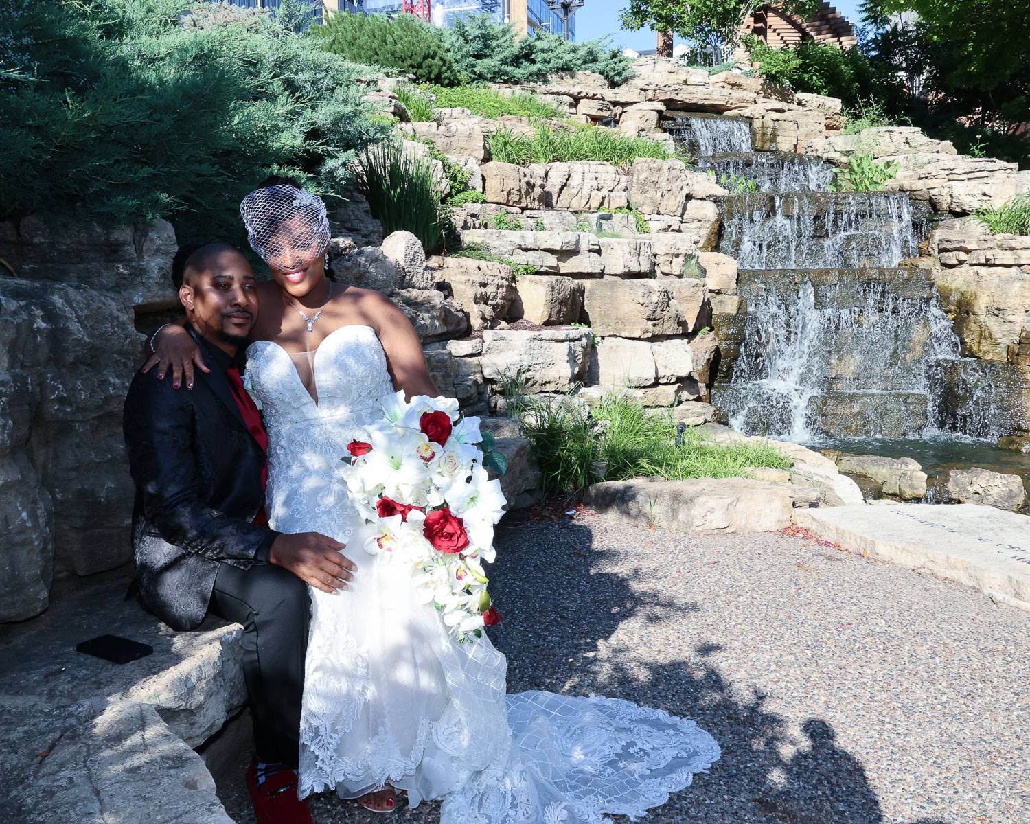 The bride and groom sitting on a stone surface near a waterfall