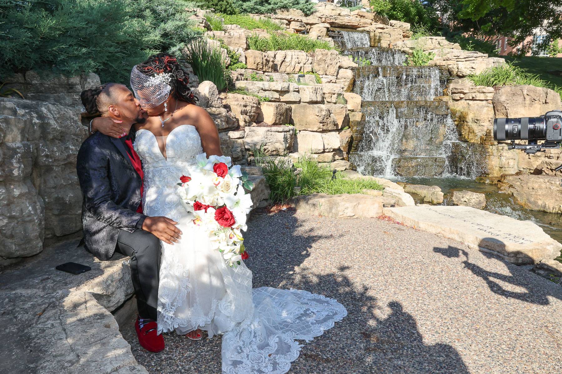 The newlyweds kiss while sitting on a stone surface